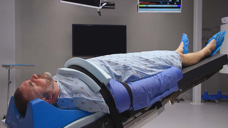 A man laying on a hospital bed in front of a television.