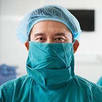 A surgeon wearing blue scrubs and a surgical mask.